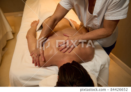 Ayurvedic treatment, professional therapeutic body massage at the wellness spa clinic. A young man relaxes while lying on a massage table during a therapeutic back massage at a luxury spa. 84426652