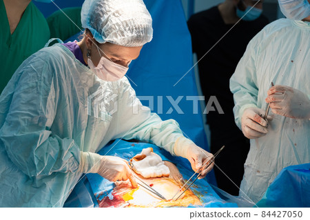 A woman surgeon performs a surgical operation on a patient's body. 84427050