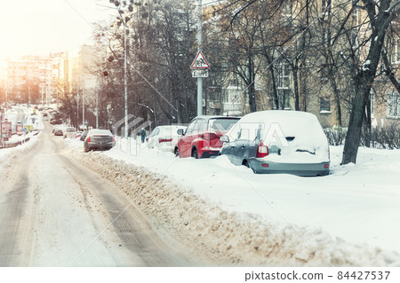 Empty city road covered by dirt melted snow sludge after heavy snowfall against street building cityscape warm sunset sun light. Cold season bad weather extreme driving conditions. Slippery driveway 84427537