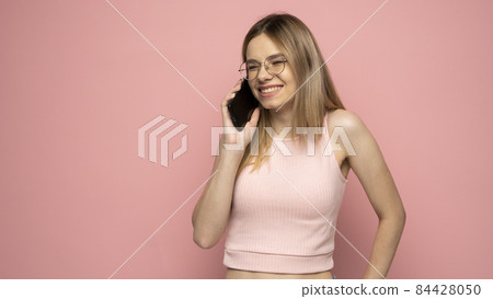 Portrait of beautiful girl wearing yellow shirt and holding mobile phone isolated over yellow background. 84428050