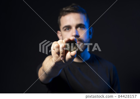 A young bearded man is holding excited a bitcoin looking at the camera. BTC the new virtual money. 84428157