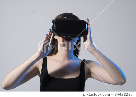 Business woman wearing VR goggles and interacts with metaverse using swipe and stretching gestures. Woman using virtual reality glasses in a studio. Business woman wearing VR goggles and interacts with metaverse using swipe and stretching gestures. Woman using virtual reality glasses in a studio. 84428283