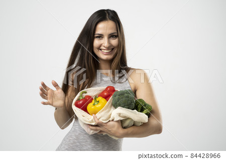 Portreit of young smiling good-looking pretty girl use mesh bag for shopping. Conscious consumption. Eco trend. Zero waste concept. Girl in dress carry bag shopper. Portreit of young smiling good-looking pretty girl use mesh bag for shopping. Conscious consumption. Eco trend. Zero waste concept. Girl in dress carry bag shopper. 84428966