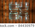 2 glasses with water and reflections on an orange checkered background 84430979