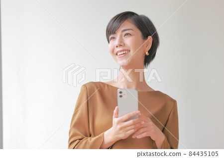 A woman holding a smartphone and looking into the distance 1 84435105
