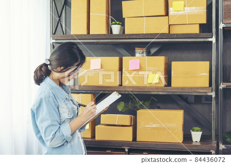 Woman checking stock goods supply delivery package shipping use document checklist. Asian woman startup small business at home office. Online entrepreneur asian woman use tablet checking online order 84436072