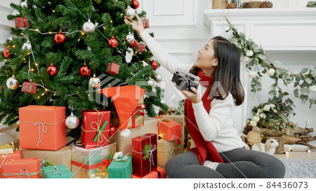 Asian woman using camera take photo christmas tree xmas present gift box in cozy living room. Woman Photographer take photo christmas decorate bauble ball xmas tree on holiday winter season celebrate Asian woman using camera take photo christmas tree xmas present gift box in cozy living room. Woman Photographer take photo christmas decorate bauble ball xmas tree on holiday winter season celebrate 84436073