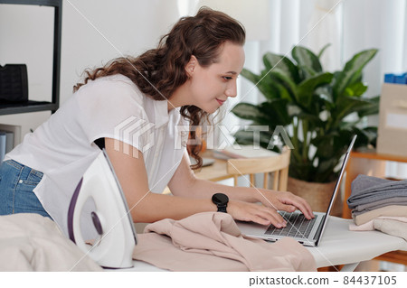 Woman Ironing and typing on Laptop 84437105
