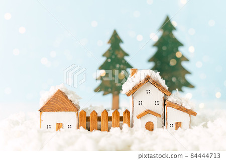 Happy New Year and Merry Christmas postcard. Festive blue background with toy wooden house, snow, light bokeh, christmas tree, village and decoration. Copy space for winter holidays greeting card 84444713