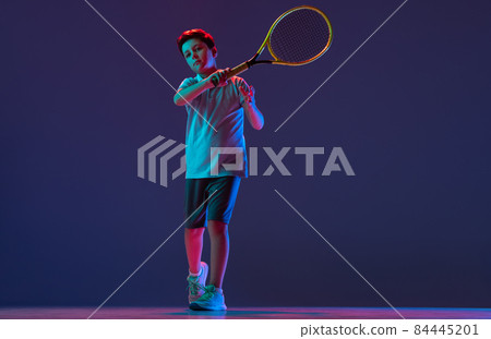 Full-length portrait of boy, playing tennis, tennis isolated over blue background in neon lights Full-length portrait of boy, playing tennis, tennis isolated over blue background in neon lights 84445201