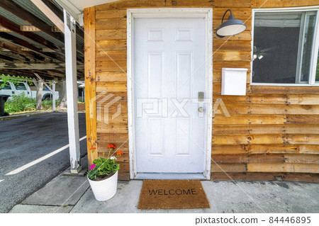 White front door decorated with flowers on a pot and doormat with welcome sign White front door decorated with flowers on a pot and doormat with welcome sign 84446895