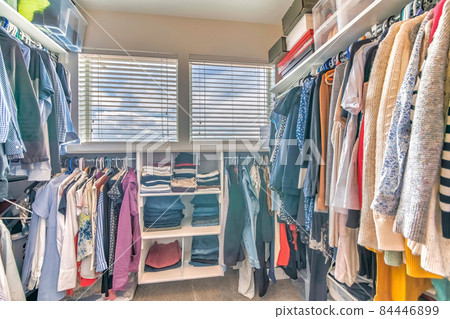 Walk in closet interior with hanging clothes and a view of a cloudy sky through the windows 84446899