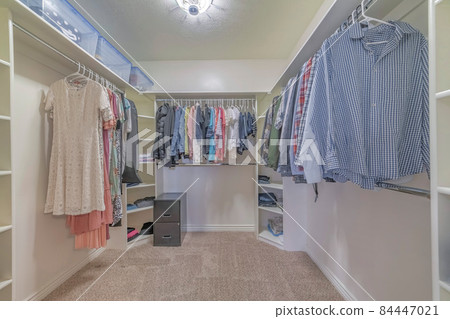 Interior of a walk in closet with shelving units and clothes 84447021