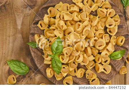 Tortellini on a wooden board with basil and parmesan. Specialties of the cuisine from Bologna and 84447232