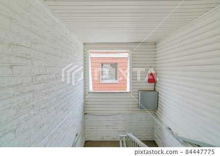 White wall with square window with a view of a window and hallway from the building across White wall with square window with a view of a window and hallway from the building across 84447775