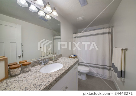 Interior of a plain white bathroom with matching gray and white shower curtain and towel 84448271
