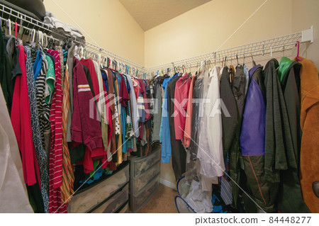 Small walk in closet with hanging colorful clothes on a metal rods 84448277
