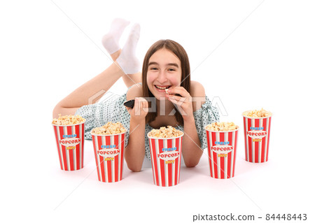 Girl lies on the floor with buckets of popcorn.. Isolated on white. 84448443