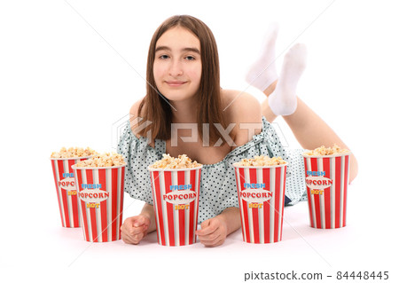Girl lies on the floor with buckets of popcorn.. Isolated on white. 84448445