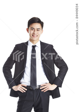 studio portrait of young asian business man arms akimbo looking at camera smiling isolated on white 84449034