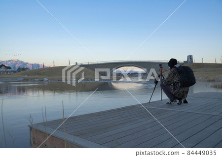 Docks of a river where a person is on it and taking a record of the place with a tripod. 84449035