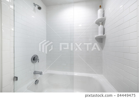 Alcove bathtub with glass wall divider and a wall with white tiles Alcove bathtub with glass wall divider and a wall with white tiles 84449475