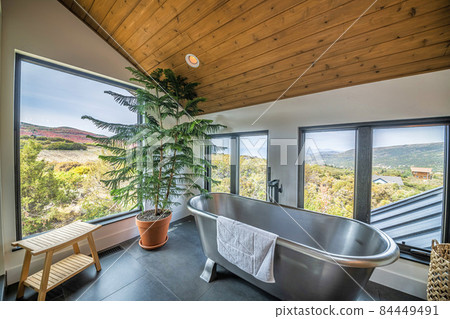 Bathroom interior with slope wooden ceiling and stainless steel bathtub with floor mounted faucet Bathroom interior with slope wooden ceiling and stainless steel bathtub with floor mounted faucet 84449491