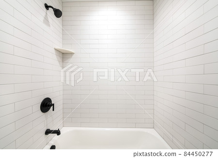 Alcove bathtub with black plumbing fixtures and white subway tiles wall surround Alcove bathtub with black plumbing fixtures and white subway tiles wall surround 84450277