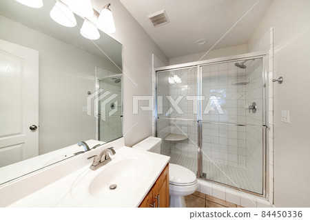 Interior of a bathroom with wooden vanity sink with tile counter and shower stall with glass 84450336