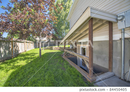 Separate basement apartment entrance with stairs, glass panel and trees on the lawn at the side 84450405