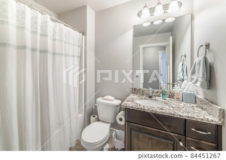 Bathroom interior with shower curtain, toilet bowl and wooden vanity with marble top 84451267