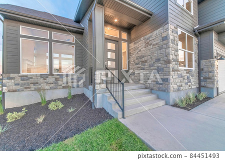 Two storey home facade with stone brick wall and glass paned gray front door 84451493