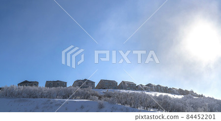 Clear, bright and sunny on a winter day shining on a field covered in snow with a row of houses on the background 84452201