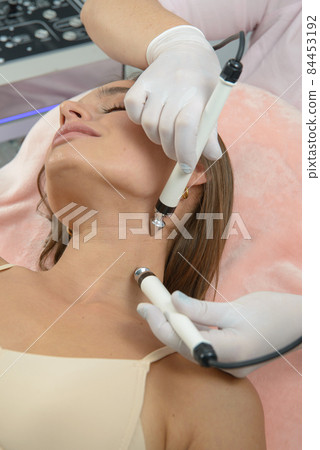 Beautiful woman at spa clinic receiving stimulating electric facial treatment from therapist. Closeup of female face during microcurrent therapy. Beautiful woman at spa clinic receiving stimulating electric facial treatment from therapist. Closeup of female face during microcurrent therapy. 84453192