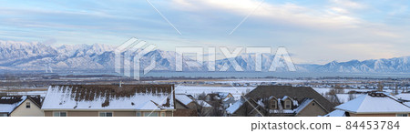 A view of the snow-covered mountains behind some house roofs 84453784