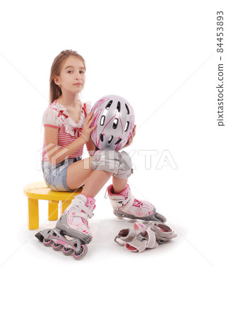 Charming broun-haired girl of school age in short jeans shorts and a pink t-shirt sitting on the chair and tries to foot roller skates. Charming broun-haired girl of school age in short jeans shorts and a pink t-shirt sitting on the chair and tries to foot roller skates. 84453893