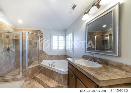 Traditional bathroom interior with vanity and corner bathtub against jalousie windows 84454080