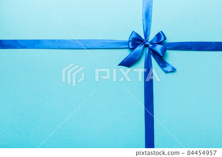 Top view of blue ribbon rolled and blue bow isolated on colored background. Flat lay with copy space 84454957