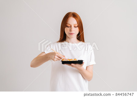 Studio shot of attractive young woman holding delicious sushi rolls with chopsticks standing on white isolated background. 84456747