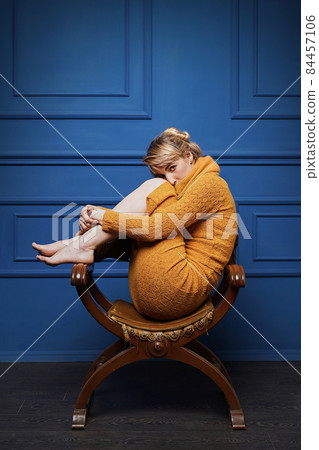 Young woman curled up in an old armchair 84457106