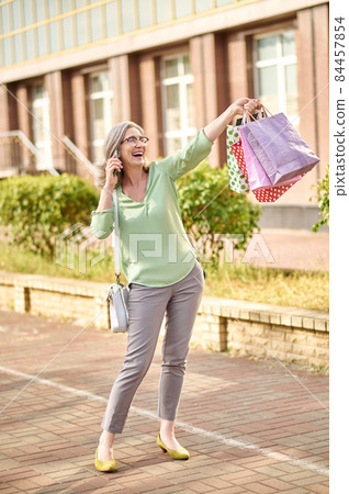 Woman raising hand with purchases talking on smartphone 84457854