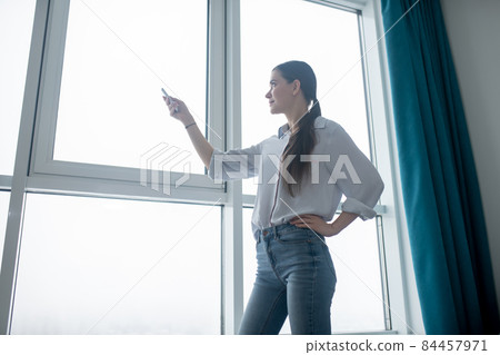 Concentrated lady using a remote control for closing the blinds Concentrated lady using a remote control for closing the blinds 84457971