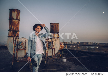 Urban man with hat and skateboard. Good looking. Cool guy. Wearing white shirt and jeans. Old neglected building in the background 84460476