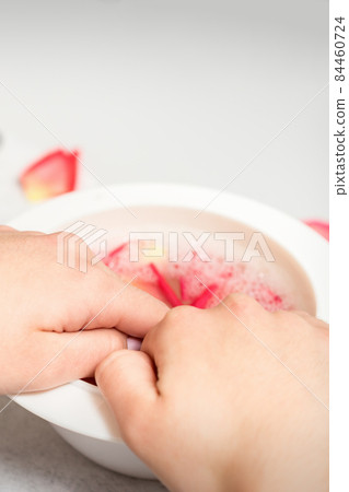Hands in white bowl bathe nails with water and rose petals to soften the cuticle and dry skin. Hands in white bowl bathe nails with water and rose petals to soften the cuticle and dry skin. 84460724