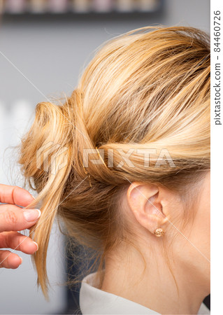 Close-up hairdresser styling blonde hair on the back of the head in a beauty salon. Close-up hairdresser styling blonde hair on the back of the head in a beauty salon. 84460726