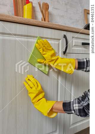 Hands in gloves with green rag is cleaning kitchen cabinets - housework and housekeeping concept Hands in gloves with green rag is cleaning kitchen cabinets - housework and housekeeping concept 84461351