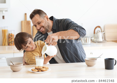 Favorite morning drink. Happy little boy helping his father to pour milk into glass, enjoying healthy breakfast at home 84461548