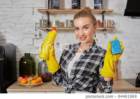Professional young woman wearing rubber protective yellow gloves holding bottle cleaners in the kitchen. Professional young woman wearing rubber protective yellow gloves holding bottle cleaners in the kitchen. 84461869