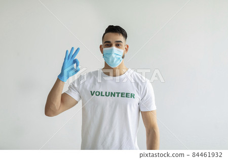 Voluntary free work, charity grace concept. Male volunteer in medical mask and gloves showing OK gesture, light wall 84461932