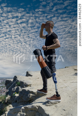 a man on a prosthetic leg travels the mountains. Dressed in black jeans and a T-shirt, he carrying mat 84462629